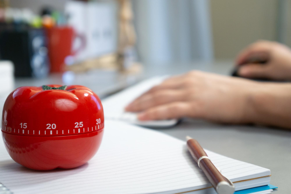 tiro de foco raso de um cronometro em forma de tomate e notebook sobre a mesa