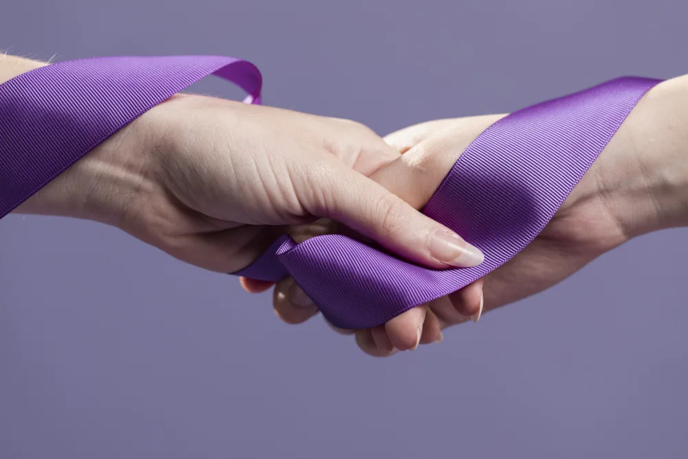 duas mão segurando laço roxo para lembrar janeiro roxo